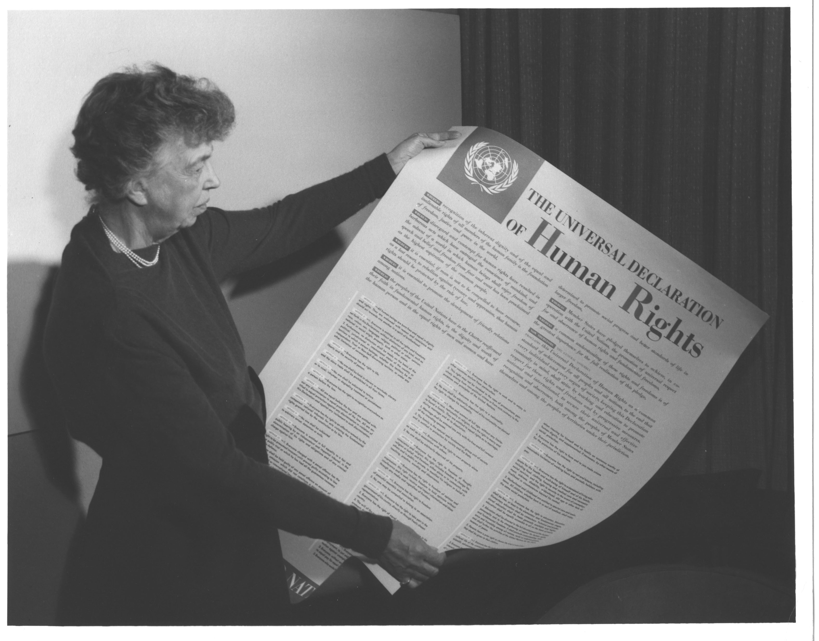Eleanor Roosevelt seated and holding an open printed copy of the Universal Declaration of Human Rights.